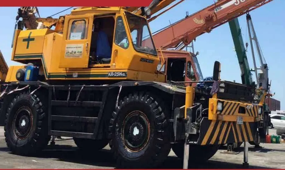 A yellow KATO KR-25H rough-terrain crane on a port quay with other crane booms raised behind it.